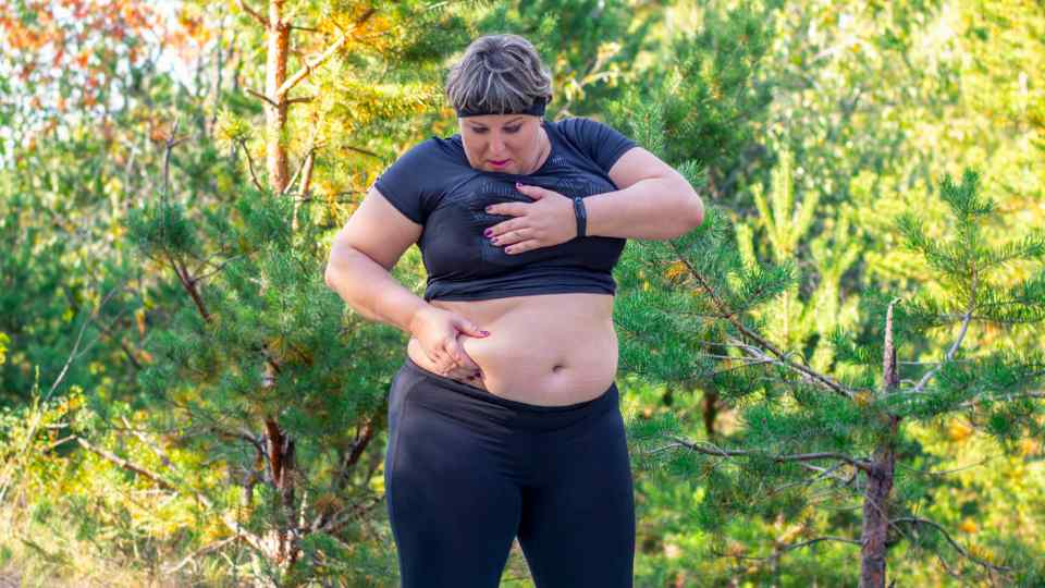 Obese woman assessing weight loss outside in gym wear